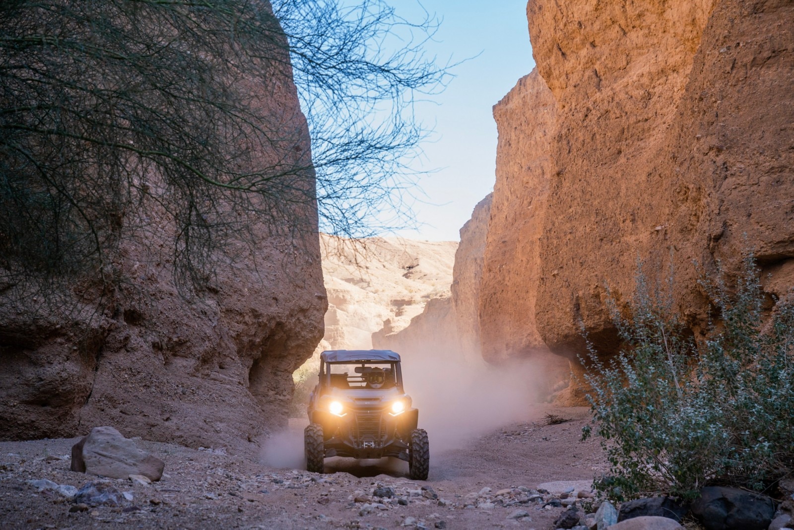 Front view of a Can-Am Defender driving between two rock walls in a desert setting